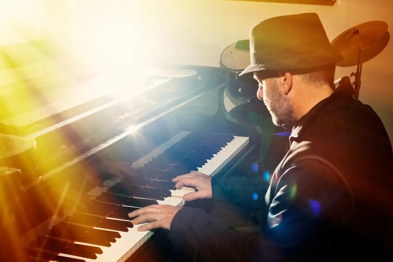 A man in black jacket playing piano with sun shining.